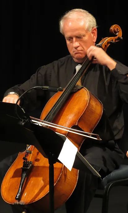 older man playing a cello in an orchestra