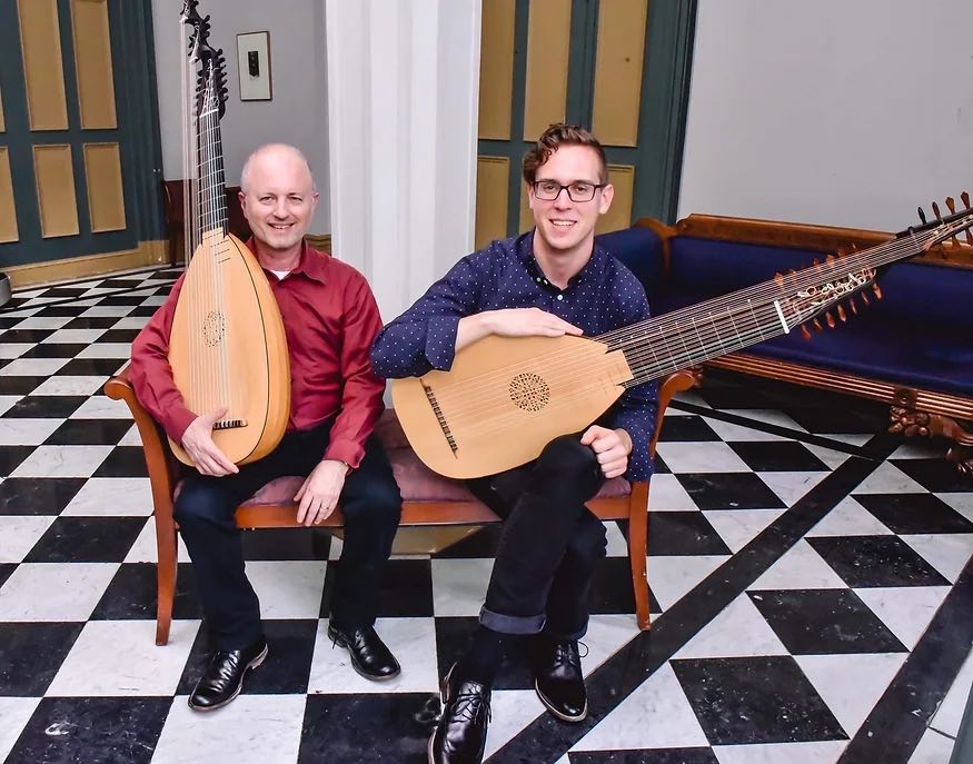 two men sitting on a bench holding lutes