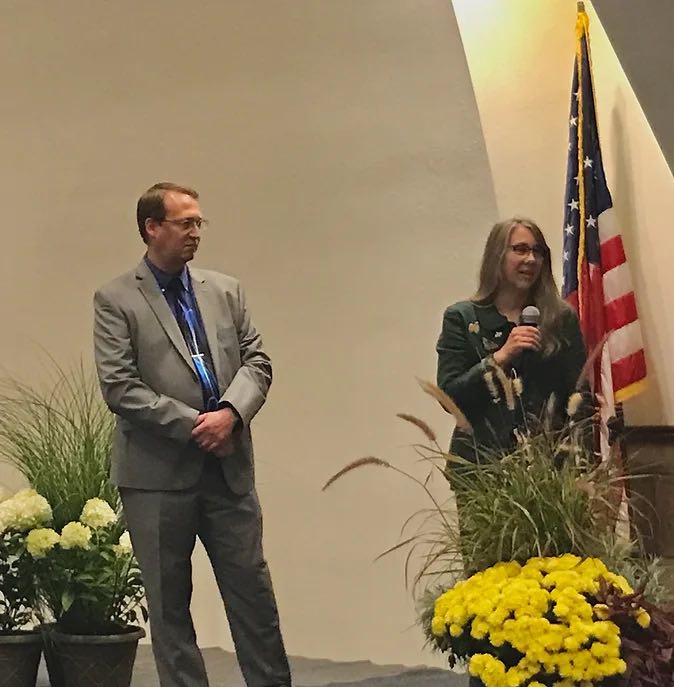 woman speaking into microphone and man holding his hands together next to her