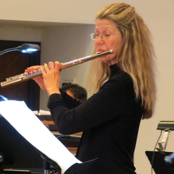 woman with long blonde hair and glasses playing a clarinet