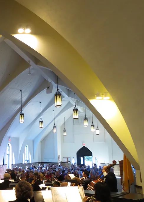 view of orchestra and audience in church with pendant lights hanging from a high ceiling