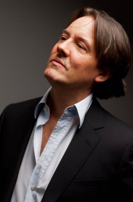 Pianist Mark Markham, clean shaven man with medium length hair wearing a button up shirt and blazer