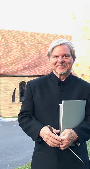 smiling older man with conductor baton and books in hands