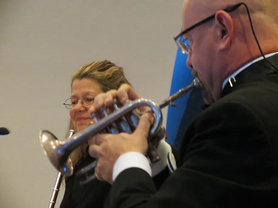 closeup of man playing a trumpet with woman holding a flute in background