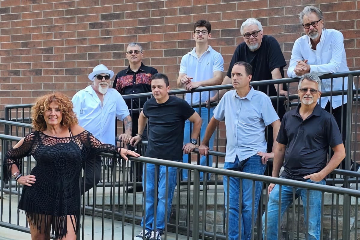 8 men and 1 woman posing on two angles of a ramp in front of a brick wall