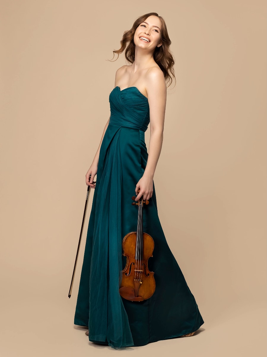 violinist Geneva Lewis in a long dark green dress holding her violin and bow