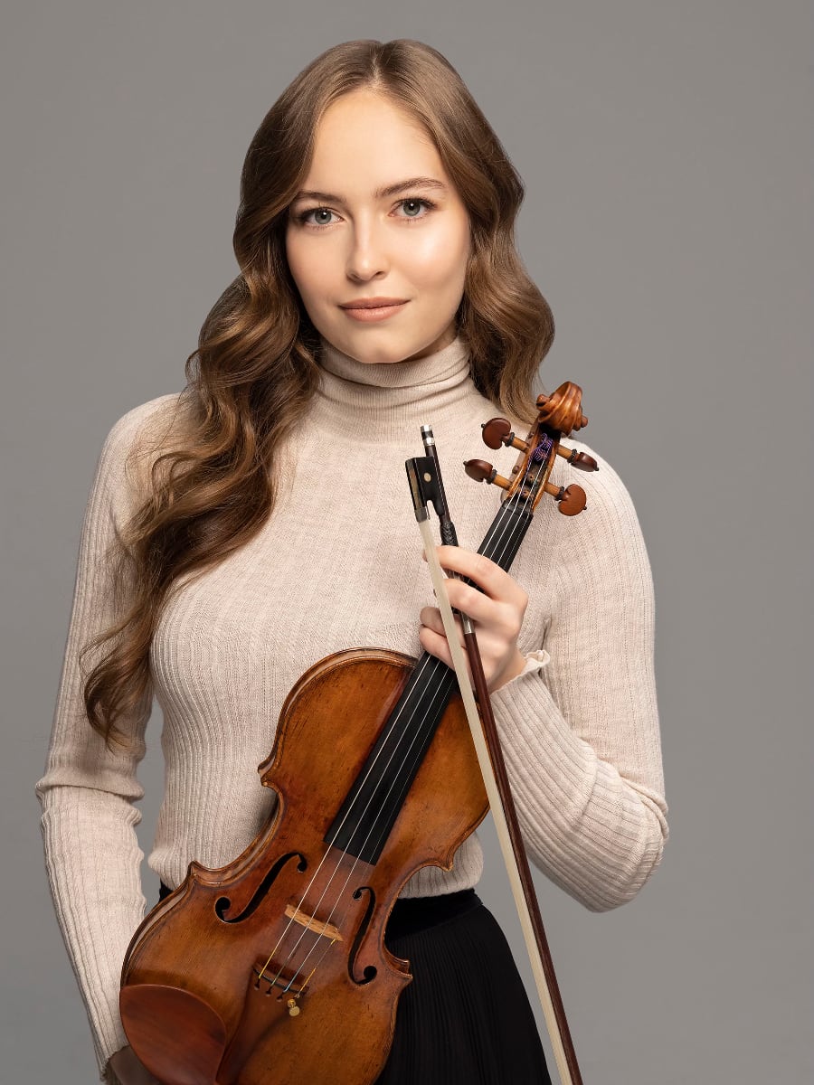 violinist Geneva Lewis in a beige turtleneck holding her violin