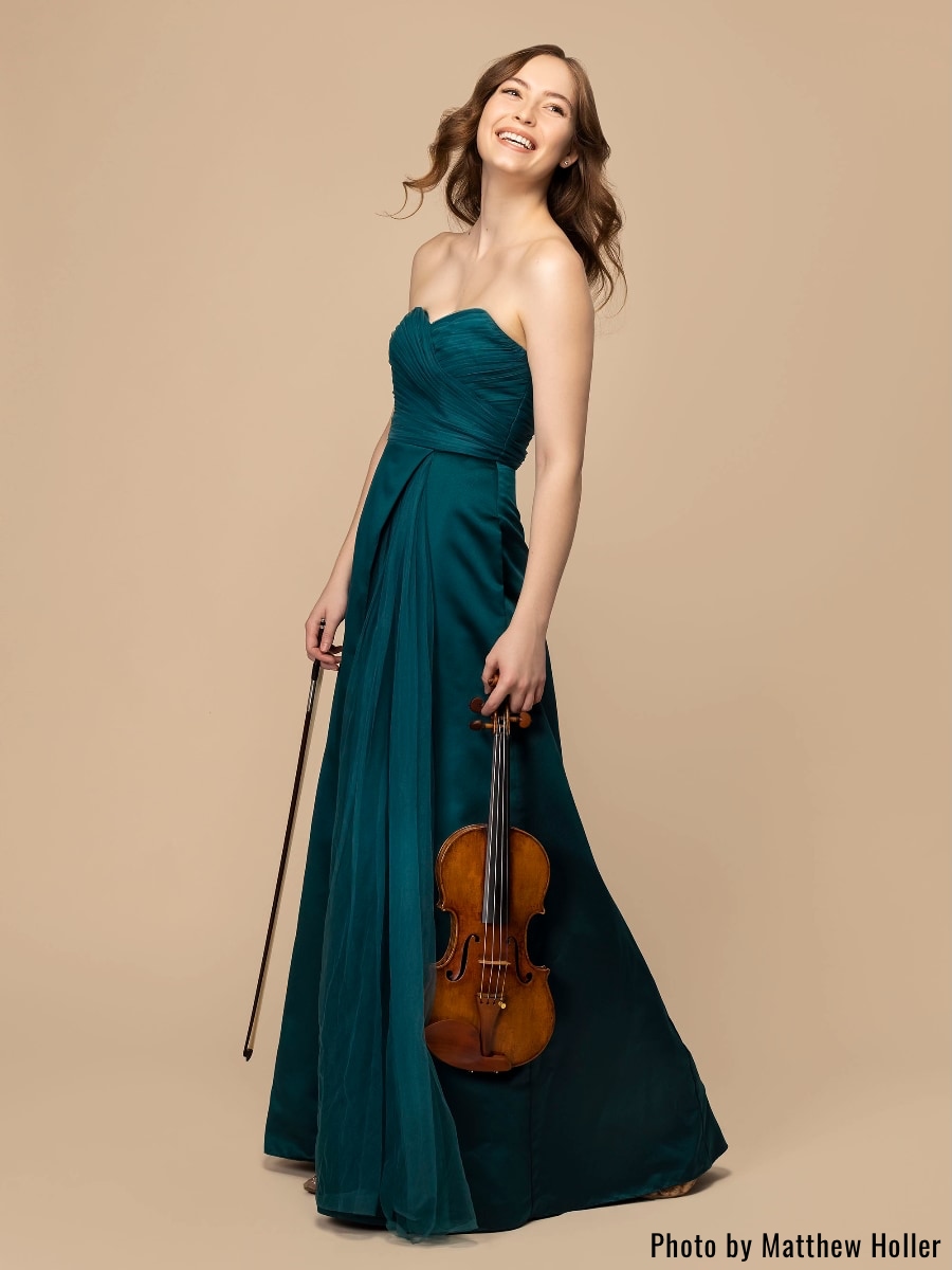 violinist Geneva Lewis in a long dark green dress holding her violin and bow; photo courtesy Matthew Holler