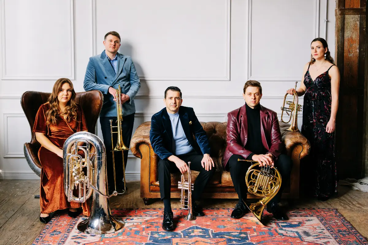 5 members of Axiom Brass holding their instruments in a room with vintage furniture