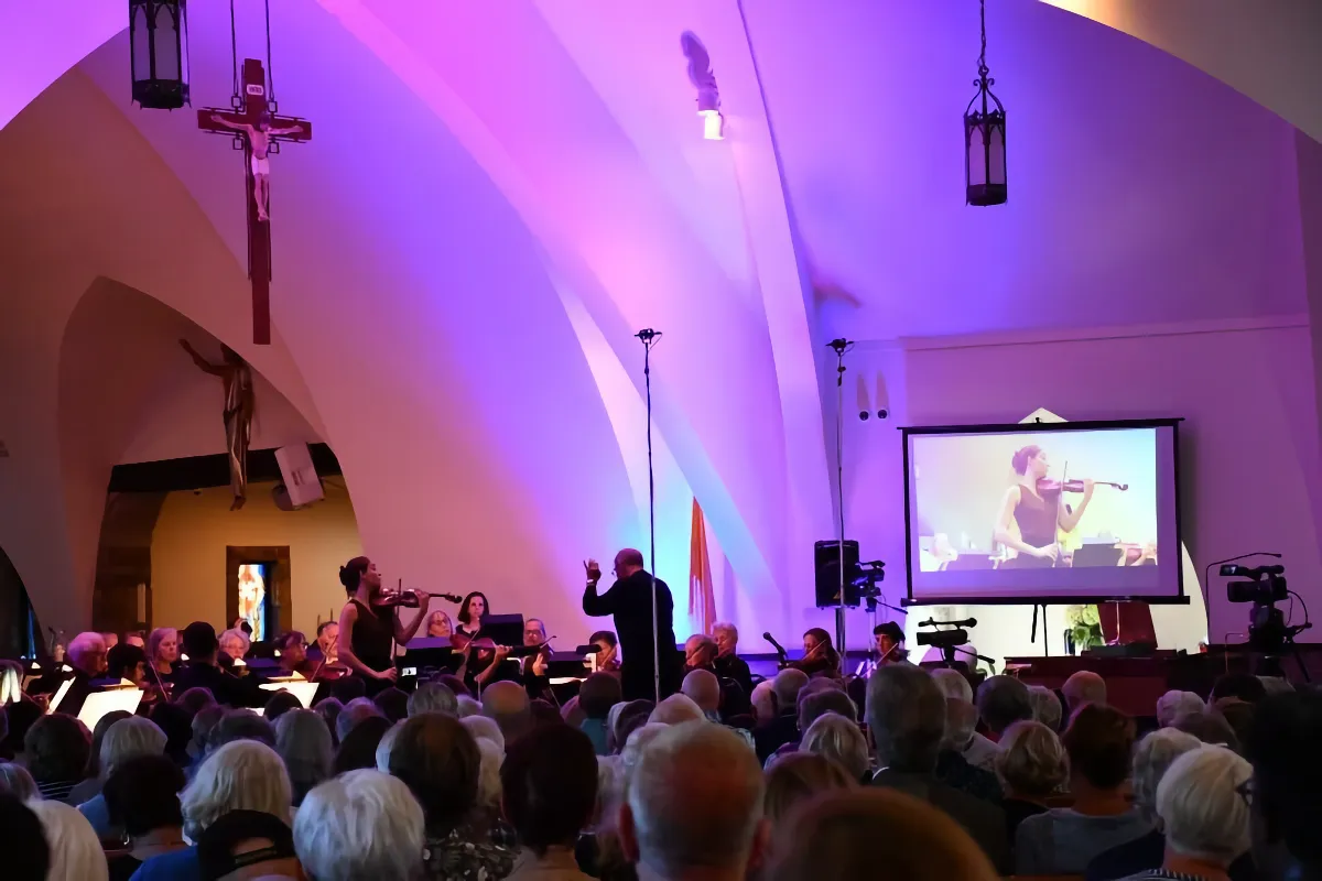 John Dodson conducting, Geneva Lewis playing violin, and Bach Festival Orchestra playing in St. Denis Church with crowd in foreground